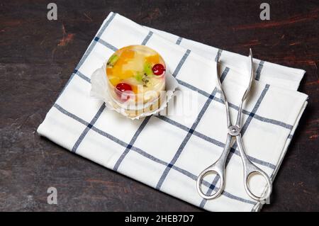 Torta con gelatina, kiwi, ciliegie e mango sul tavolo. Mini dessert yummy su sfondo di legno, primo piano. Foto Stock