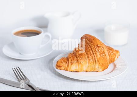 Croissant in un ambiente bianco luminoso, con una tazza di caffè e latte e altri croissant in uno sfondo sfocato. Ambiente colazione semplice ed elegante Foto Stock