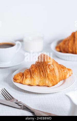 Croissant in un ambiente bianco luminoso, con una tazza di caffè e latte e altri croissant in uno sfondo sfocato. Ambiente colazione semplice ed elegante Foto Stock