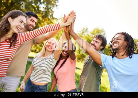 Gruppo di giovani diversi festeggia l'integrazione e l'amicizia in natura con i cinque alti Foto Stock