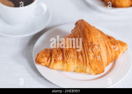 Croissant in un ambiente bianco luminoso, con una tazza di caffè e latte e altri croissant in uno sfondo sfocato. Ambiente colazione semplice ed elegante Foto Stock