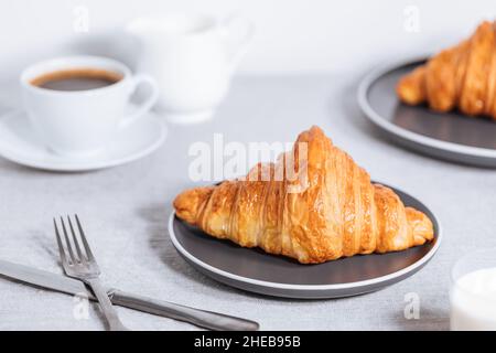 Croissant in un ambiente bianco luminoso, con una tazza di caffè e latte e altri croissant in uno sfondo sfocato. Ambiente colazione semplice ed elegante Foto Stock