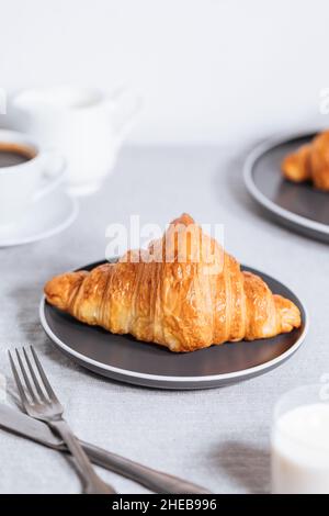 Croissant in un ambiente bianco luminoso, con una tazza di caffè e latte e altri croissant in uno sfondo sfocato. Ambiente colazione semplice ed elegante Foto Stock