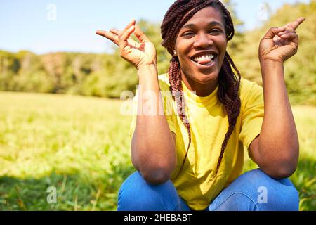 Giovane donna fiduciosa con trecce Rasta su un prato in estate con gesti freddi Foto Stock