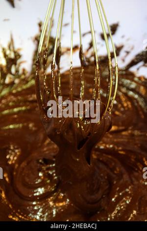 Fare il cioccolato a casa. Liquido e scuro su sfondo sfocato montato con una frusta in una piastra di plastica Foto Stock