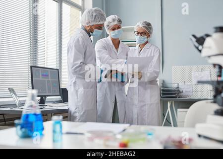 Gruppo di scienziati in possesso di un documento di protezione e discutere i risultati dell'analisi in team presso il laboratorio Foto Stock