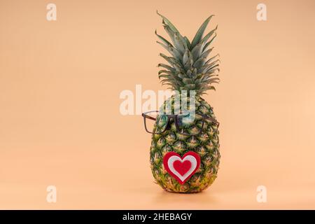 Interpretazione della frutta di ananas nell'immagine umana con i vetri e il concetto di cuore della medicina o degli amanti di giorno di San Valentino. Spazio di copia su sfondo giallo Foto Stock