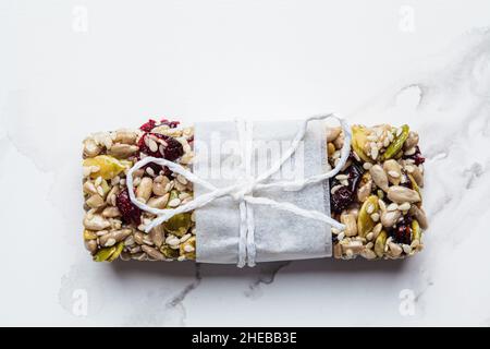 Barra di granola energetica con semi di zucca, semi di sesamo e mirtilli su sfondo di marmo bianco, vista dall'alto. Concetto di snack sano. Foto Stock