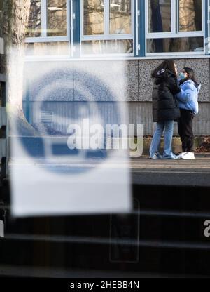 10 gennaio 2022, bassa Sassonia, Osnabrück: Un cartello "le maschere sono obbligatorie" è appiccicato su una porta della scuola secondaria di Möser a Westerberg. Gli allievi con le maschere chirurgiche stanno in piedi nel cortile di rottura. Con l'inizio della scuola dopo le vacanze di Natale, un obbligo quotidiano di prova comincia per gli allievi nel nuovo anno. In futuro, gli studenti di età inferiore ai 14 anni dovranno indossare una maschera OP o FFP2; una maschera di tessuto non sarà più sufficiente. Foto: Friso Gentsch/dpa Foto Stock