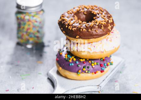Selezione di ciambelle con colori diversi su sfondo grigio con bicchiere di latte Foto Stock
