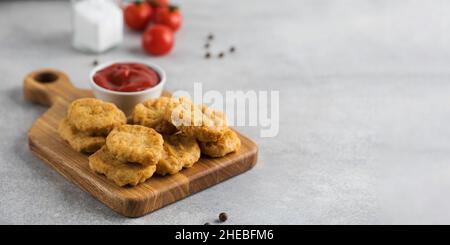 Pepite di pollo dorate in un asse di legno, cosparse di cipolle verdi e un ketchup. Spazio di copia. Foto Stock