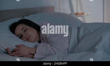 Donna brunetta in pigiama che dorme a letto a casa Foto Stock