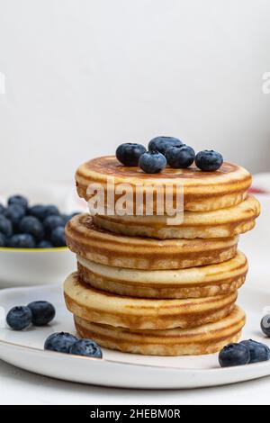 Accatastate deliziose frittelle sul piatto bianco con mirtilli freschi su e nel recipiente. Vista laterale, spazio di copia Foto Stock