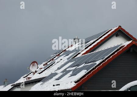 Il tetto in tegole della casa con pannelli solari è coperto di neve Foto Stock