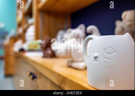 Fila di figure in ceramica grezza non finita su uno scaffale di studio in un negozio fai da te per la pittura. Foto Stock