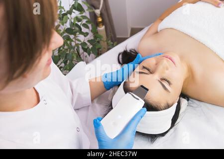 Specialista cosmetologo fare trattamento di procedura facciale a una donna paziente utilizzando ultrasuoni pelle attrezzature. Foto Stock