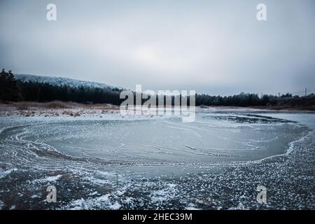 Splendido lago ghiacciato con strati concentrici di ghiaccio con grumi di neve, Foresta sullo sfondo, incredibile paesaggio invernale, splendida vista Foto Stock