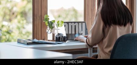 Vista posteriore della giovane donna d'affari asiatica seduta sul suo posto di lavoro in ufficio. Giovane donna che lavora per i grafici dei dati dei documenti finanziari con il laptop in Foto Stock