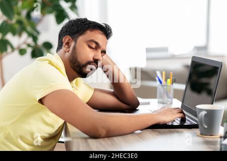uomo indiano che dorme sul tavolo con un computer portatile a casa Foto Stock