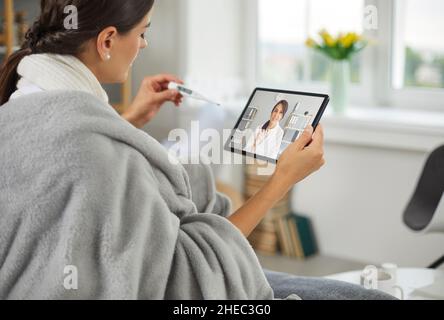 La donna che ha febbre sta avendo telemedicina consultazione con il medico online su tablet Foto Stock