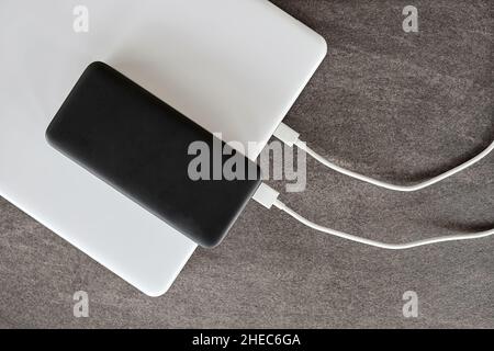 Power Bank ricarica un computer portatile tramite cavo USB di tipo C su sfondo grigio in pietra Foto Stock