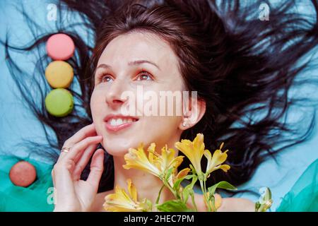 La giovane donna faccia da vicino con fiori e macaron francesi da vicino. Concetto di National Macaroon Day. Foto estive colorate. Foto Stock