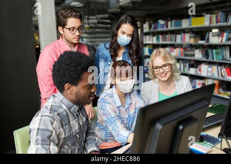 studenti in maschere mediche con computer in biblioteca Foto Stock