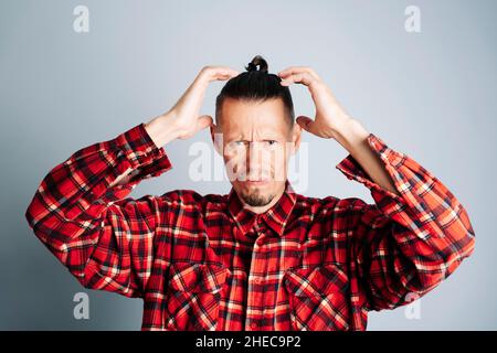Un uomo bearded in una camicia rossa della plaid tocca la sua testa. Un uomo ha un mal di testa, un uomo ha stress, su sfondo blu Foto Stock