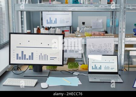 Immagine di computer con grafica sullo schermo e provette con campioni sugli scaffali per esperimenti scientifici in laboratorio Foto Stock