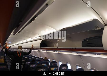 Membro dell'equipaggio di cabina che chiude le porte su armadietto passeggeri a soffitto / armadietti / compartimento / compartimenti per stivare passeggeri borse bagagli di cabina, su un aereo Easyjet Airbus A320 o A319. (128) Foto Stock