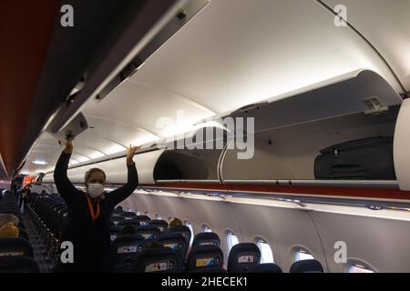 Membro dell'equipaggio di cabina che chiude le porte su armadietto passeggeri a soffitto / armadietti / compartimento / compartimenti per stivare passeggeri borse bagagli di cabina, su un aereo Easyjet Airbus A320 o A319. (128) Foto Stock