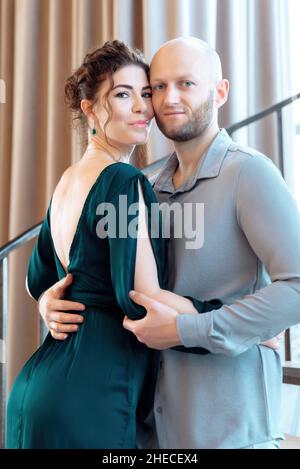 Ritratto di bella coppia giovane in posa foto ripresa in interni. Felice coppia amorevole. Donna ricurly attraente e uomo barbuto elegante. Scatto verticale Foto Stock
