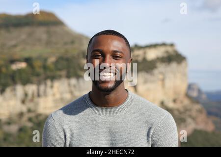 Vista frontale ritratto di un uomo felice con pelle nera sorridente alla macchina fotografica in montagna Foto Stock