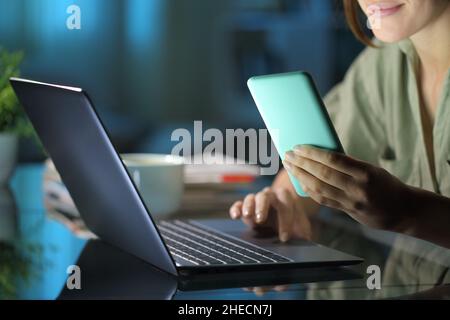 Primo piano di una donna che usa il telefono e il computer portatile di notte a casa Foto Stock