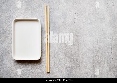 Piastra rettangolare vuota e bacchette di bambù su sfondo grigio con spazio di copia Foto Stock