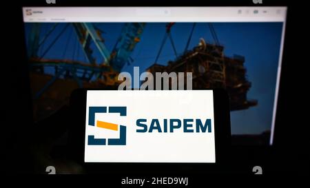 Persona che detiene il cellulare con il logo della società italiana Saipem S.p.A. di servizi petroliferi sullo schermo di fronte alla pagina web. Mettere a fuoco sul display del telefono. Foto Stock