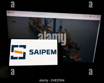 Persona che detiene il cellulare con il logo della società italiana Saipem S.p.A. di servizi petroliferi sullo schermo di fronte al sito web. Mettere a fuoco sul display del telefono. Foto Stock