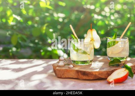 Due bicchieri di rinfrescante bevanda fresca estiva o cocktail di pere e menta con ghiaccio su sfondo di verdure. Concetto estivo. Nutrizione sana e. Foto Stock