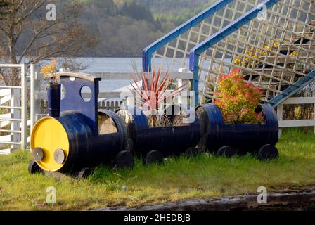 Treno ferroviario modello, fatto da vecchi tamburi e riempito di piante, su una piattaforma disutilizzata alla stazione ferroviaria di Loch awe, Loch awe, Scozia Foto Stock