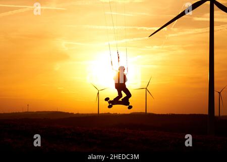 Kite terra boarder salta di fronte al tramonto del sole. 1 uomo a un'arte sportiva estrema in azione con una kiteboard. Paesaggio con turbine eoliche come silhouette. Foto Stock