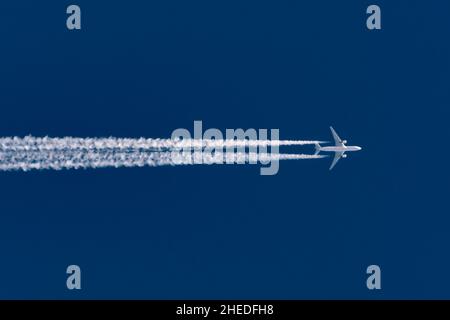 L'aeroplano vola lasciando la traccia di contrail su un cielo blu chiaro alto Foto Stock