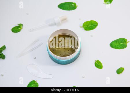 Idrogel cosmetico idratante e rinfrescante collagene cerotti occhi su sfondo bianco con foglie di menta piperita e gocce d'acqua Foto Stock