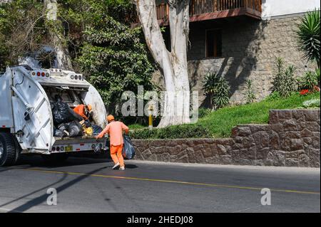 Due garbagemen lavorando insieme su bidoni di svuotamento per rimozione rifiuti Foto Stock