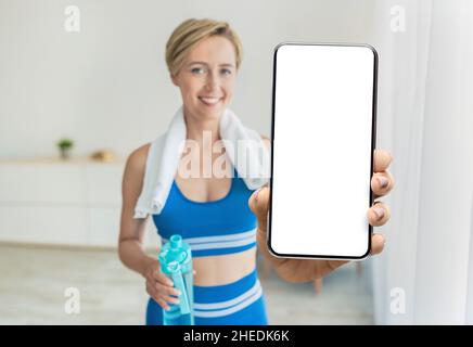 Fitness Online. Donna di mezza età sorridente in Sportswear che dimostra uno smartphone vuoto alla Camera Foto Stock
