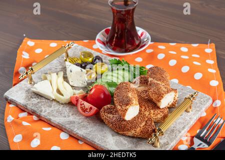 Colazione tradizionale turca con formaggio feta, verdure, olive, simit, bagel e tè su un vassoio di marmo su sfondo di legno scuro. Foto Stock