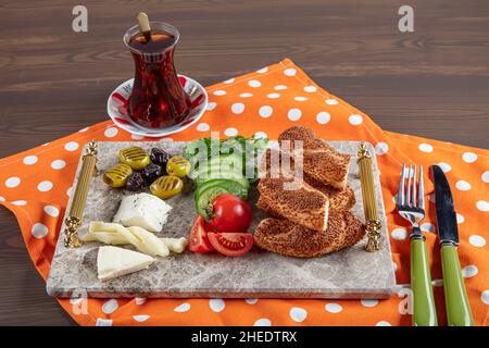 Colazione tradizionale turca con formaggio feta, verdure, olive, simit, bagel e tè su un vassoio di marmo su sfondo di legno scuro. Foto Stock