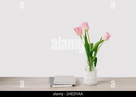 Un bouquet di tulipani rosa di fiori primaverili in vaso si trova sul desktop vicino ai taccuini. Spazio di copia Foto Stock