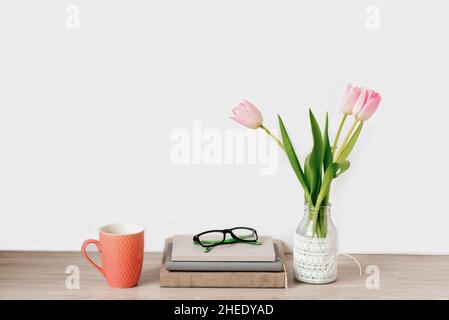 Un bouquet di tulipani rosa di fiori primaverili in vaso si trova sulla scrivania accanto a taccuini con bicchieri e una tazza di tè. Spazio di copia Foto Stock