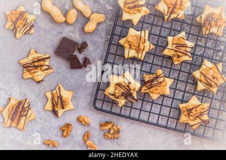 Biscotti fatti in casa a forma di stella con guarnizione al caramello al nocciola e cioccolato, su una griglia rinfrescante e sfondo grigio, vista dall'alto Foto Stock