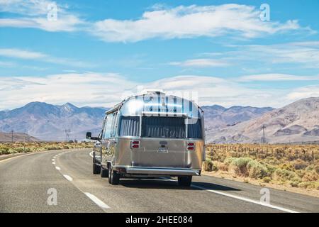 California USA 05-01-2021-Airstream Camper su autostrada a due corsie che attraversa il pennello da montagna verso la catena montuosa con linee elettriche alte - vista posteriore. Foto Stock